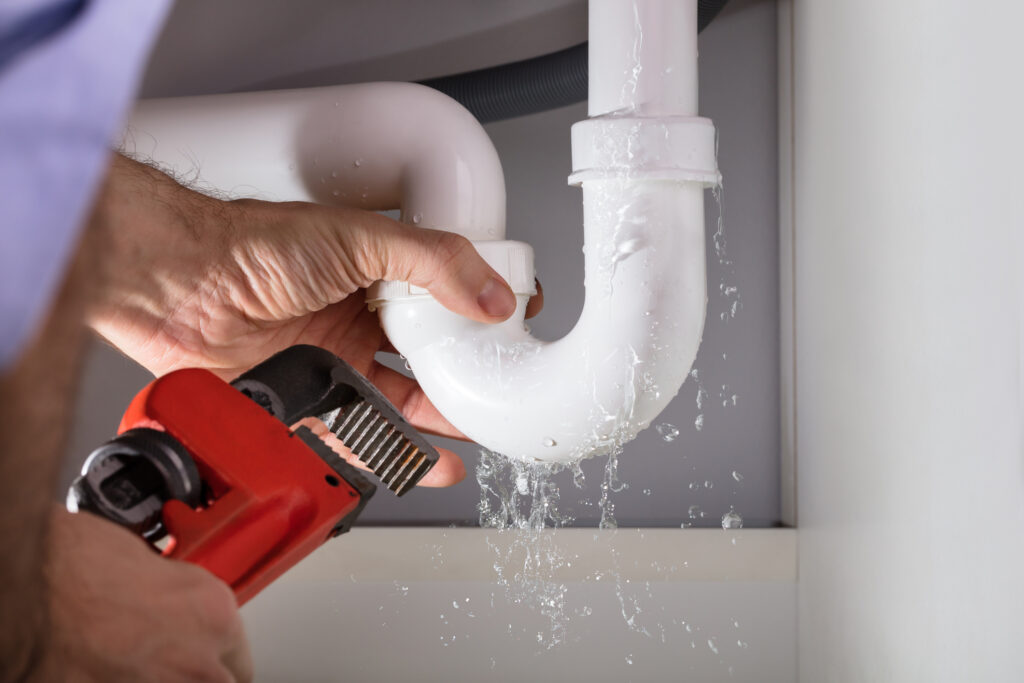 Close-up of plumber's hands holding a red wrench, fixing white sink pipe that's leaking water.